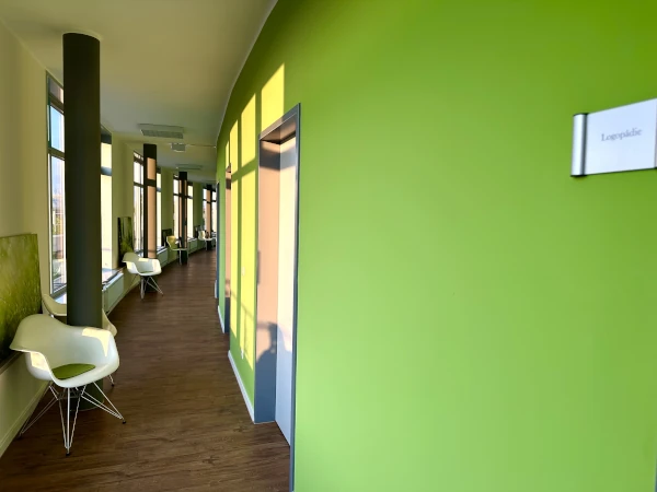 Ansicht Innen, langer Gang mit grüner Wand, brauner Boden und Sitzgelegenheiten